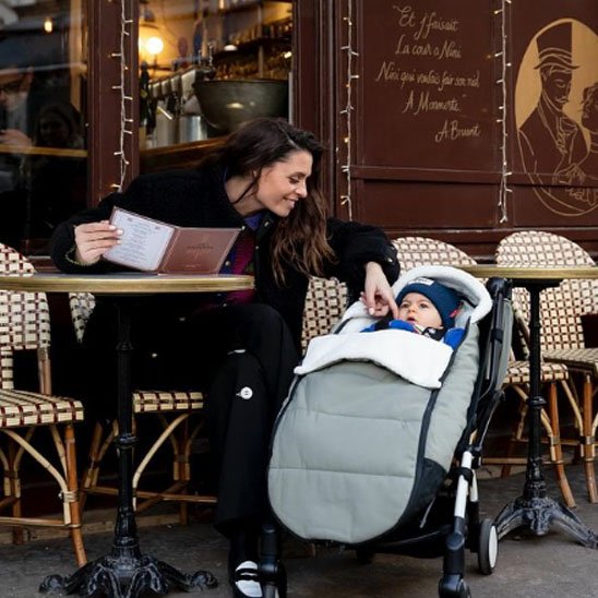 Chanceliere poussette grise et maman assise au caféria joue avec son bébé