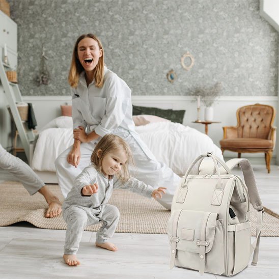 sac à dos à langer biege et maman joue avec son bébé dans sa chambre